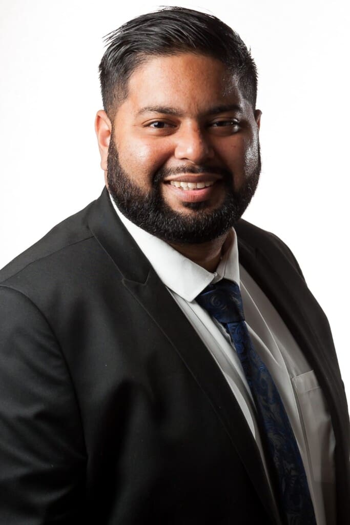 Ridhwaan Basa, founder of Tenacious Property, smiling in a dark suit and tie — professional headshot