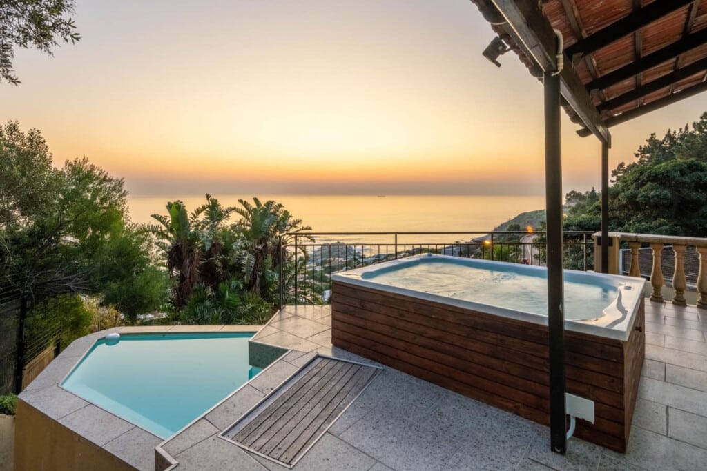 Private pool and hot tub on a tiled terrace overlooking lush gardens and the ocean at sunset, Cape Town vacation rental